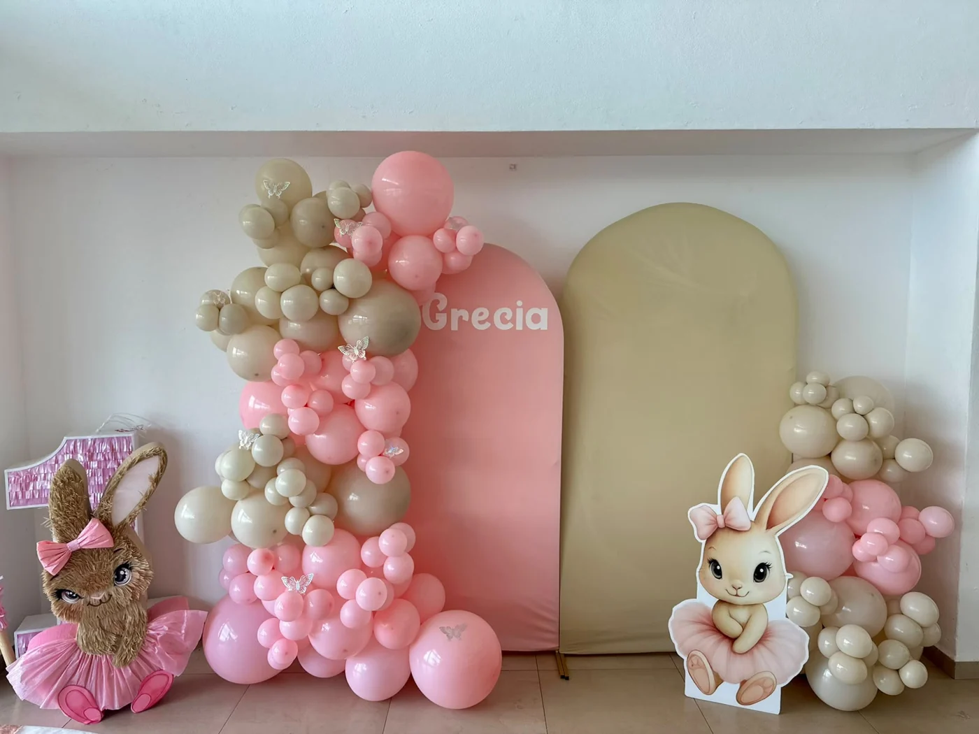 Montaje de cumpleaños con globos rosa y crema, mesa de pastel y paneles decorados